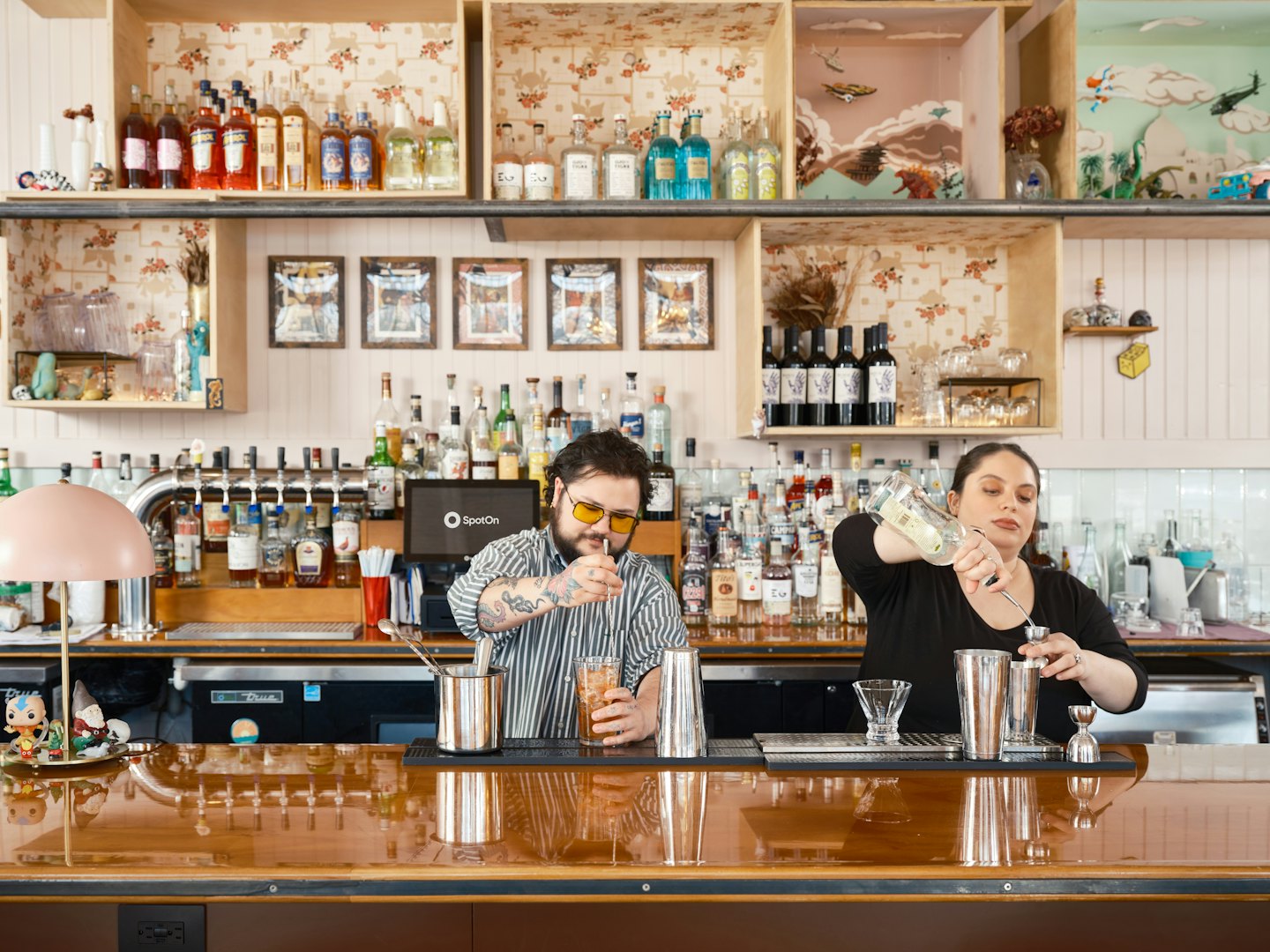 Due baristi preparano cocktail dietro un bancone di legno lucido.