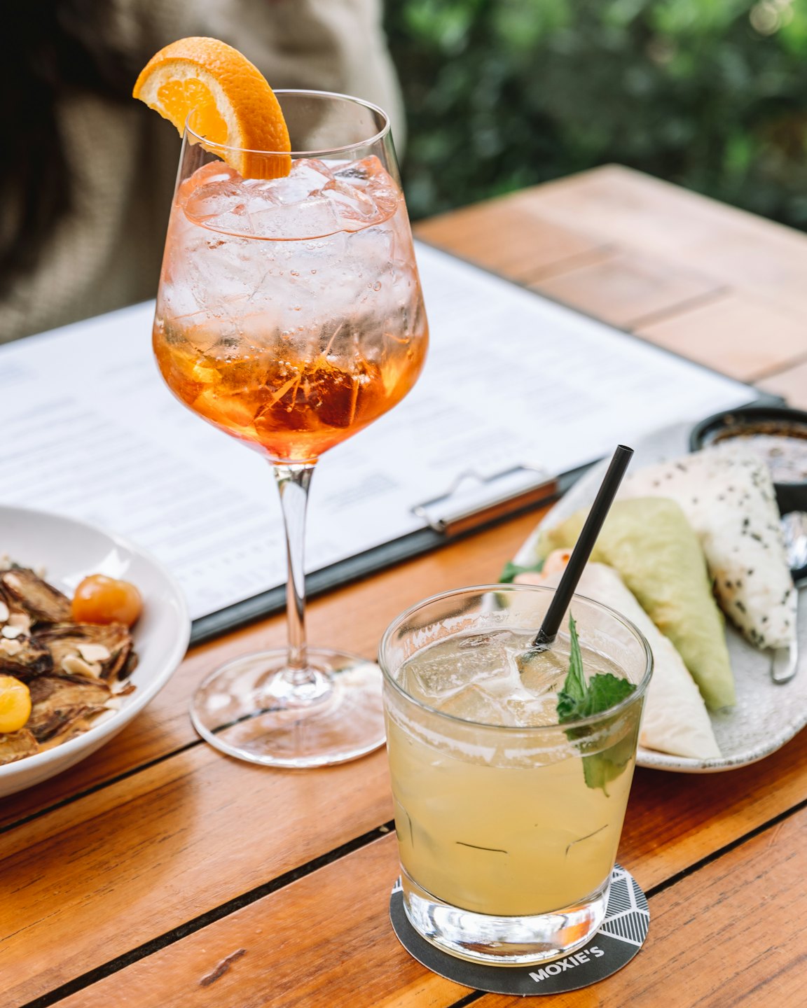 Due cocktail e antipasti su un tavolo di legno all'aperto.