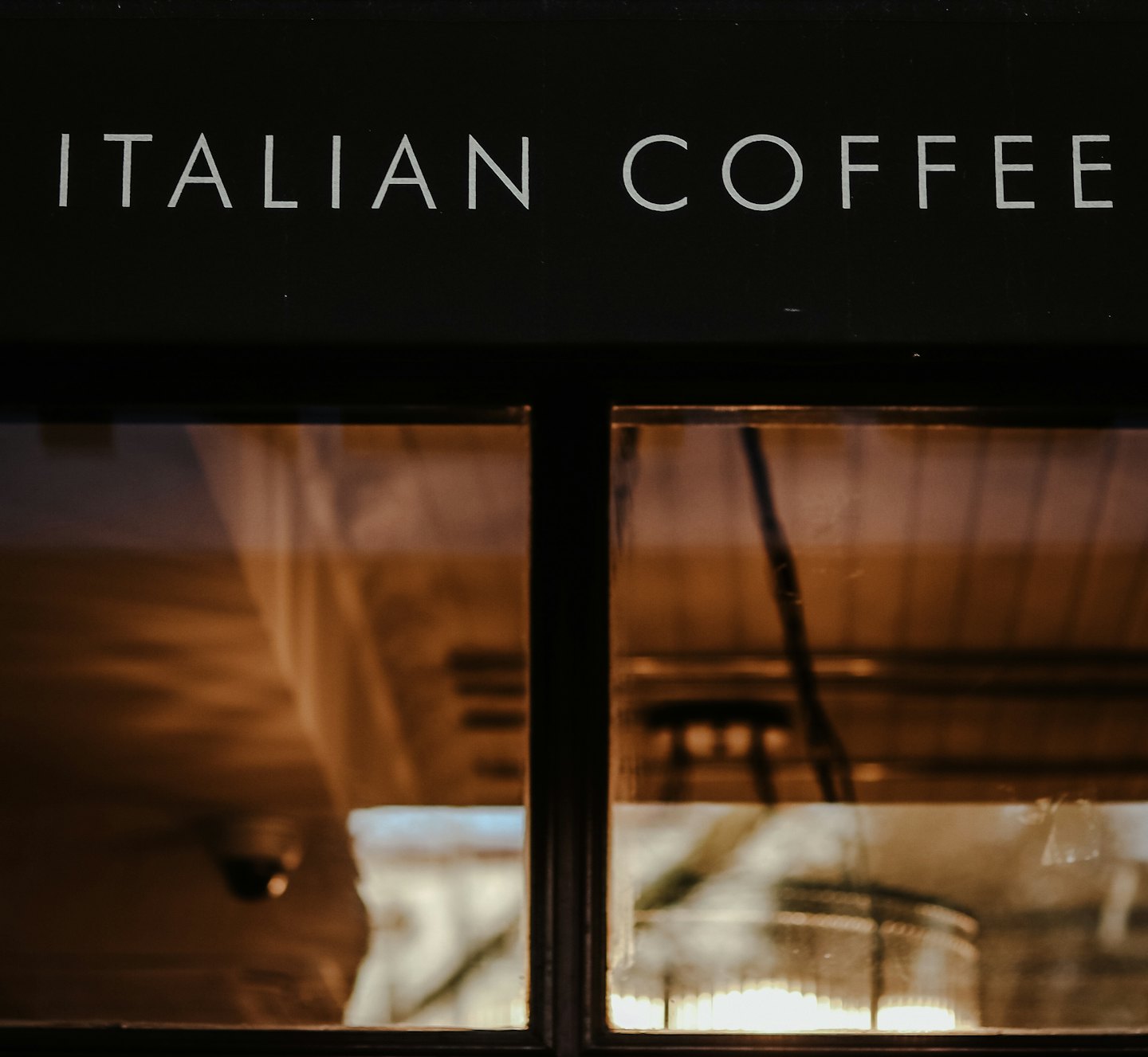 Facciata di un bar scuro con la scritta "ITALIAN COFFEE" sopra le vetrate.