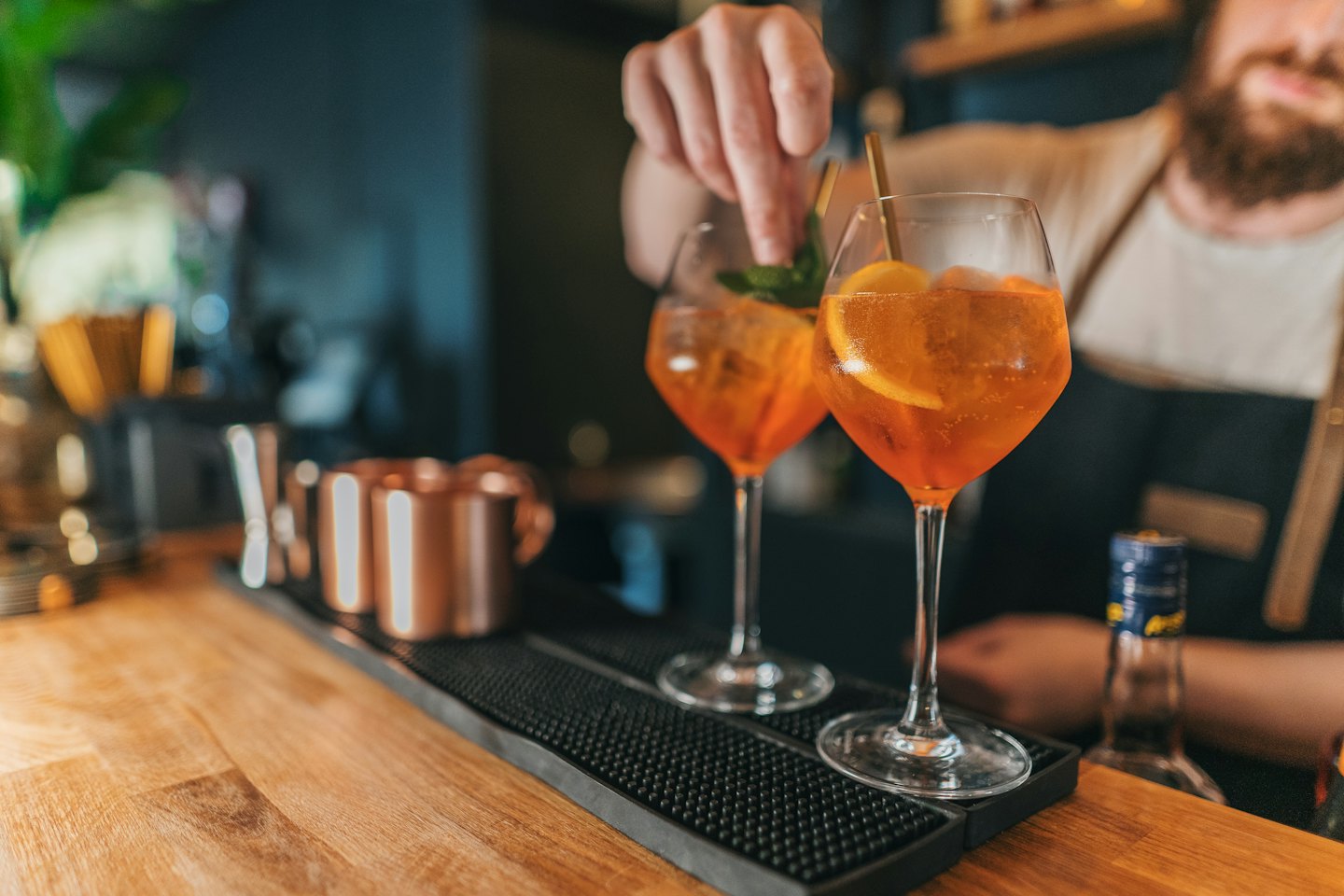 Un barista aggiunge menta fresca a un cocktail su un bancone di legno.